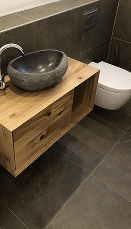 Modern bathroom vanity with a stone vessel sink, wooden cabinet, and wall-mounted toilet.