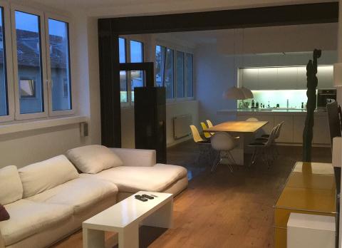 Open-plan living room and kitchen with a white sofa, dining table, and large windows.